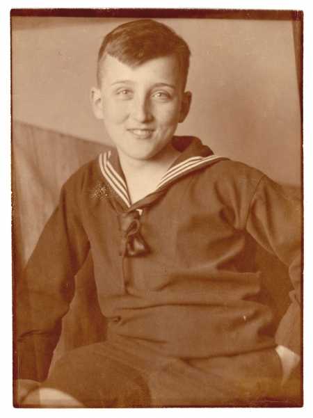 Photo de couleur sépia d'un jeune adolescent assis et souriant à la caméra. Il porte un chandail de couleur foncé avec un col marin.