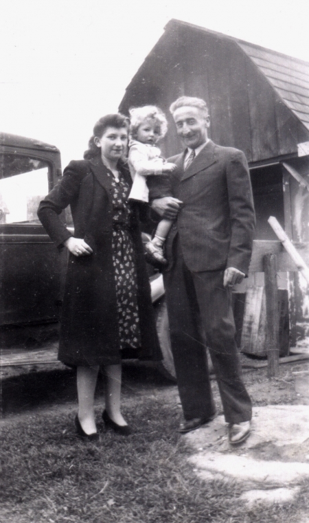 Photo en noir et blanc d'un homme et d'une femme avec un jeune enfant au cheveux blonds bouclés. Ils sont ensemble à l'extérieur devant un camion et une grange en arrière-plan.