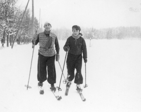 Black-and-white photograph of a woman and young boy wearing winter clothing and cross-country skiing in a snowy field.