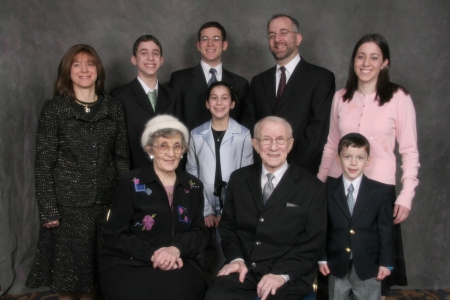 Colour studio photograph of nine people grouped together as a family in two rows, smiling at the camera.