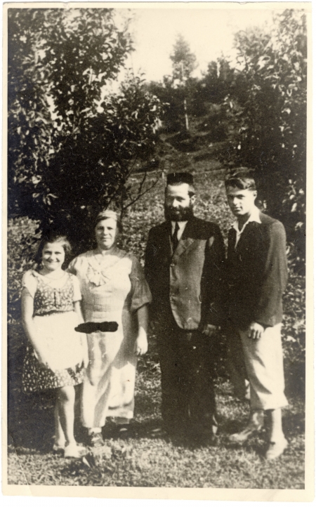 Black-and-white photograph of four people standing outdoors, with trees in the background.