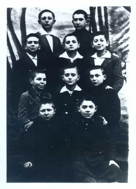 Black-and-white photograph of a group of ten young boys, posing in four rows of two or three. The boys look at the camera, most of them wearing collared shirts under jackets.