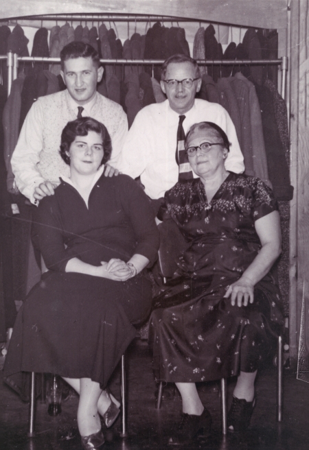 Photo en noir et blanc de deux hommes debout derrière deux femmes, assises sur des chaises. Le couple de droite semble être plus âgé que celui de gauche. Les deux hommes portent des chemises et des cravates et les femmes des robes.