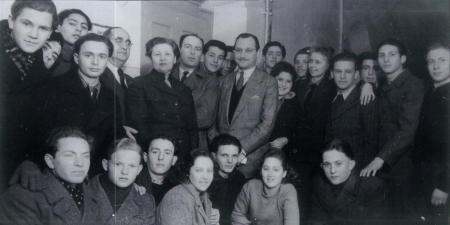 Black-and-white photograph of a large group of about thirty youth, grouped in two rows and smiling at the camera. An older man in a suit stands in the middle of the group.