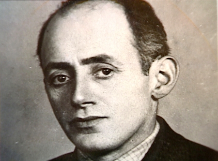 Black-and-white portrait photograph depicting the face of a man, looking at the camera. He wears his dark hair combed back, and he appears to be wearing a suit.