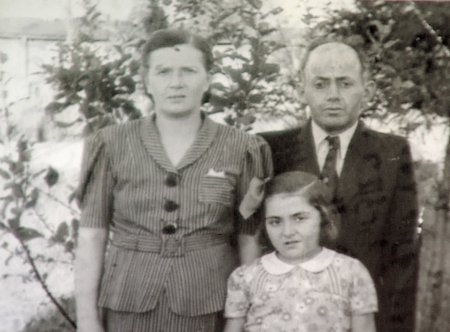 Black-and-white photograph of a man and woman with their young daughter, standing outdoors with trees in the background. The man wears a suit and the woman and young girl wear blouses.