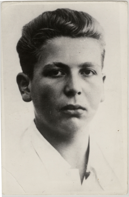 Black-and-white portrait photograph of a young man, approximately 15 years of age. The young man, wearing a white collar shirt with his hair brushed back, looks straight at the camera and does not smile.