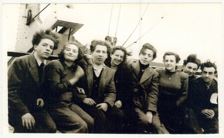 Black-and-white photograph of a group of 8 young adults, men and women, sitting together on the deck of a ship.