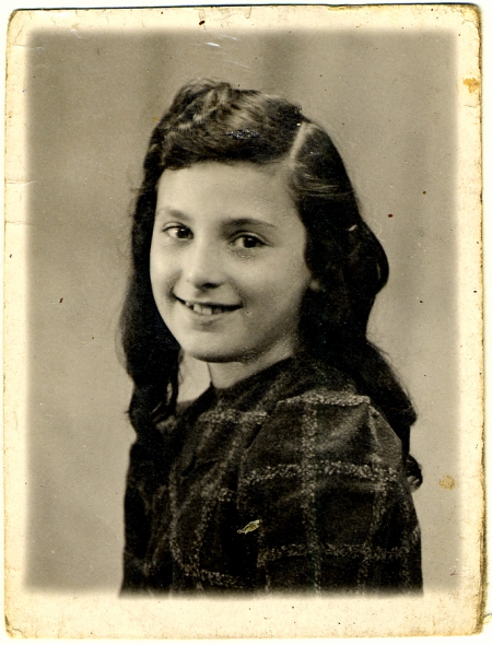 Black-and-white portrait photograph of a young girl, turning her head to smile at the camera. She has long, wavy brown hair.