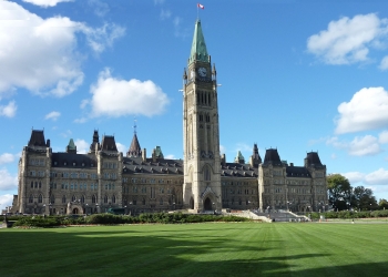 Photo couleur du parlement canadien a Ottawa avec la pelouse en avant-plan et un ciel bleu avec quelques nuages.