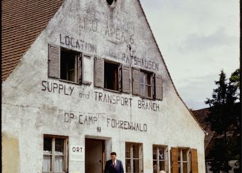 Diapositive en couleur d'une vue extérieure d'un bâtiment de trois étages. Trois hommes se tiennent devant le bâtiments.