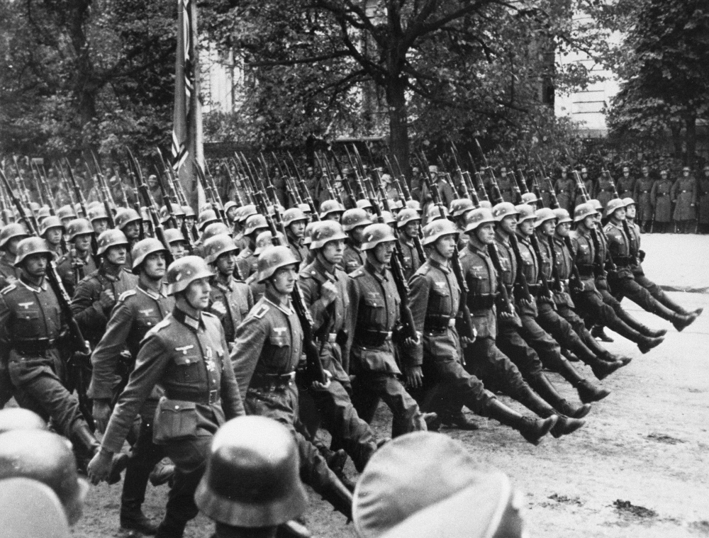 Black-and-white photograph of a large group of soldiers marching in unison on a boulevard.