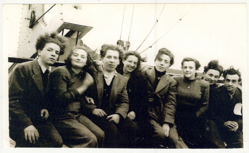 Photo d'un groupe de huit jeunes adultes, hommes et femmes, assis ensemble sur le pont  d'un navire.