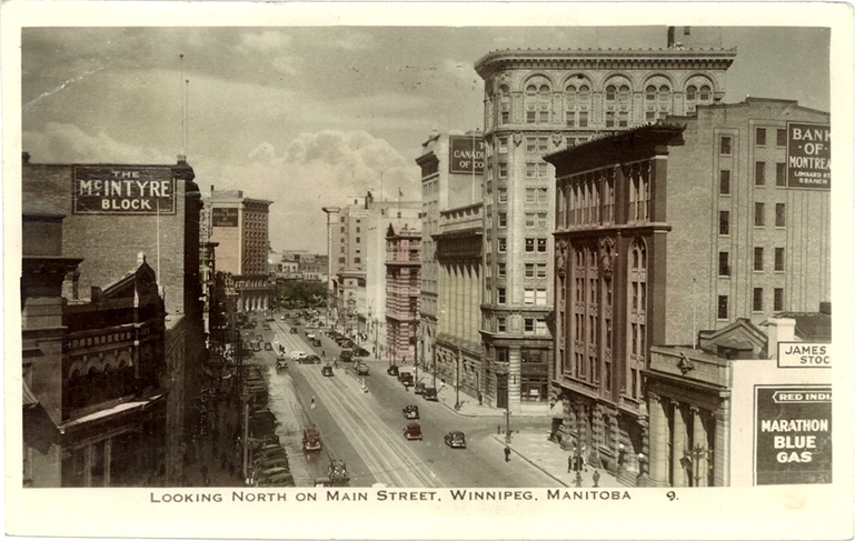 Photo en noir et blanc de bâtiments légèrement colorés en jaune et rose, représentant la vue d'une rue d'une ville où il y a des édifices en brique et des vitrines de commerces. Il y a des affiches sur trois bâtiments pour The McIntyre Block, Marathon Blue Gas et Bank of Montreal.