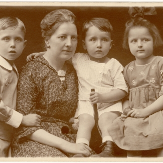 Sepia-toned portrait photograph of a woman with three young children, posing closely together in formal dress.