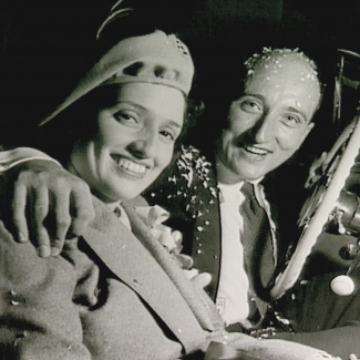 Photo en noir et blanc de forme carrée d'un homme et d'une femme assis ensemble dans une voiture, souriant. L'homme est couvert de confettis et entoure la femme de son bras.