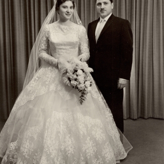 Photo en noir et blanc d'un homme et d'une femme le jour de leur mariage. La femme porte une longue robe blanche et un voile et tient un bouquet de fleurs, et l'homme porte un costume formel ainsi qu'une moustache.