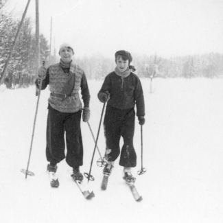 Black-and-white photograph of a woman and young boy wearing winter clothing and cross-country skiing in a snowy field.