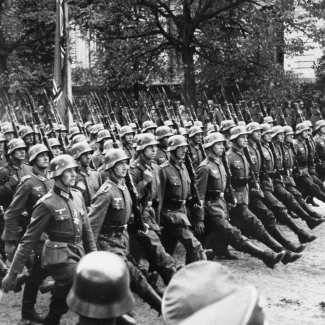 Black-and-white photograph of a large group of soldiers marching in unison on a boulevard.