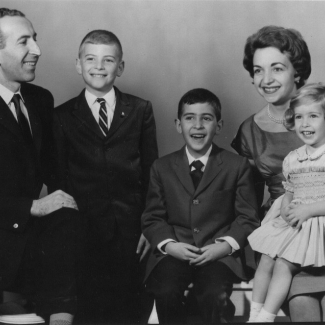 Black-and-white studio photograph of a man and woman with their three young children, smiling at the camera. The man and two boys wear suits, and the woman and her daughter are in dresses.