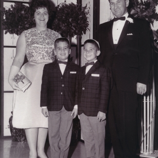 Black-and-white photograph of a man and woman with their two young sons. The family is formally dressed, the man and boys wearing suits with bowties, and the woman wears a dress.