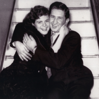 Photo en noir et blanc d'un jeune couple souriant et assis dans les bras l'un de l'autre dans un escalier.