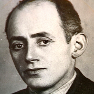 Black-and-white portrait photograph depicting the face of a man, looking at the camera. He wears his dark hair combed back, and he appears to be wearing a suit.