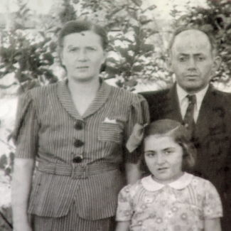 Black-and-white photograph of a man and woman with their young daughter, standing outdoors with trees in the background. The man wears a suit and the woman and young girl wear blouses.