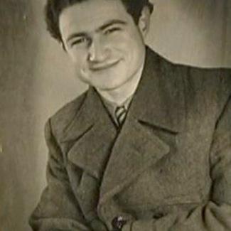 Portrait photographique d'un jeune homme, pris à partir de la taille, assis les bras croisés. Il porte un manteau et sourit à la caméra.
