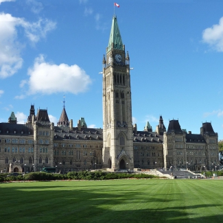 Color photo of the Canadian parliament central building with green grass at the front and a blue sky with a couple of clouds.