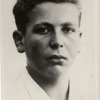 Black-and-white portrait photograph of a young man, approximately 15 years of age. The young man, wearing a white collar shirt with his hair brushed back, looks straight at the camera and does not smile.