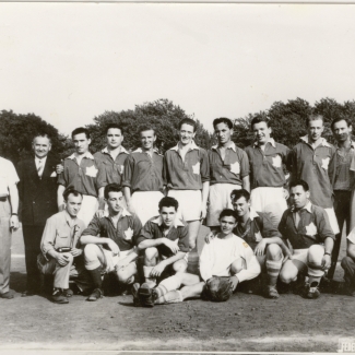 Photo en noir et blanc d'une équipe de soccer d'environ 15 jeunes hommes et quatre entraîneurs, répartis en deux rangées sur un terrain de soccer. Leur uniforme d'équipe présente un drapeau canadien sur leur poitrine.