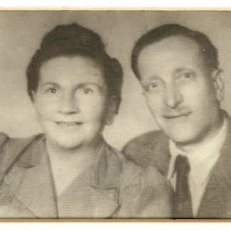 Photo en noir et blanc prise à partir du buste, d'un homme et d'une femme souriant à la caméra. L'homme porte costume et cravate et la femme a les cheveux attachés.