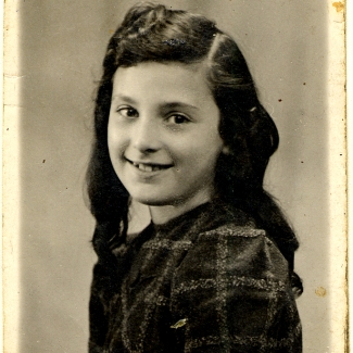 Portrait photographique en noir et blanc d'une jeune fille, la tête tournée et souriant vers la caméra. Elle a de longs cheveux bruns ondulés.