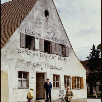 Colour slide of the exterior view of a three-storey building. Three men stand outside the building.