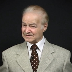 Screenshot of Leon Hirsch, Holocaust survivor, sitting in front of a grey background, and looking to the left of the camera while recording his video testimony. The camera shows his face and shoulders.