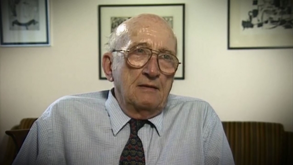 Capture d'écran du témoignage vidéo du survivant de l’Holocauste Gerhart Maass. Il est assis devant un mur blanc avec trois tableaux et regarde à la droite de la caméra. Son visage et ses épaules sont visibles à la caméra.