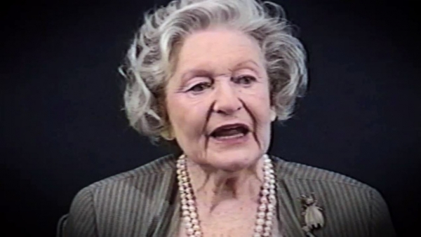 Screenshot of Holocaust survivor Irene Burstyn video testimony. She is sitting in front of a black background, and looking to the left of the camera. The camera shows her face and shoulders.