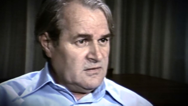 Screenshot of Holocaust survivor Aba Beer video testimony. He is sitting in front of grey curtains, and looking to the right of the camera. The camera shows his face and shoulders.