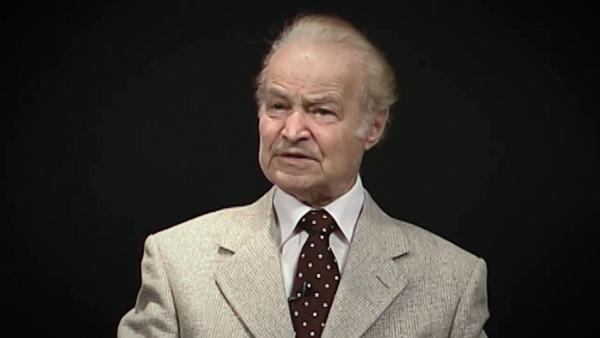 Screenshot of Leon Hirsch, Holocaust survivor, sitting in front of a grey background, and looking to the left of the camera while recording his video testimony. The camera shows his face and shoulders.