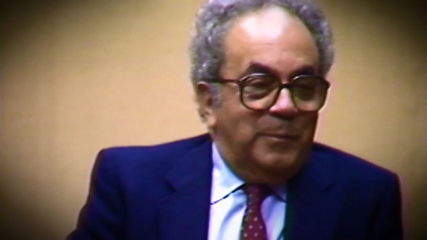 Screenshot of Holocaust survivor David Shafran video testimony. He is sitting in front of a beige background, and looking to the right of the camera. The camera shows his face and shoulders.