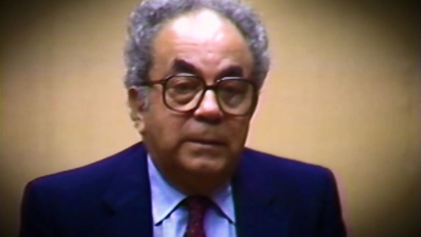 Screenshot of Holocaust survivor David Shafran video testimony. He is sitting in front of a beige background, and looking to the right of the camera. The camera shows his face and shoulders.